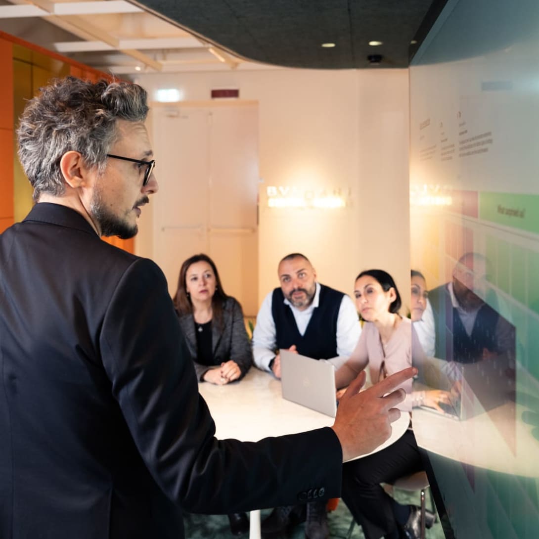 Nicola, responsable de dominio de datos en Bvlgari, señalando una pizarra mientras explica a tres compañeros