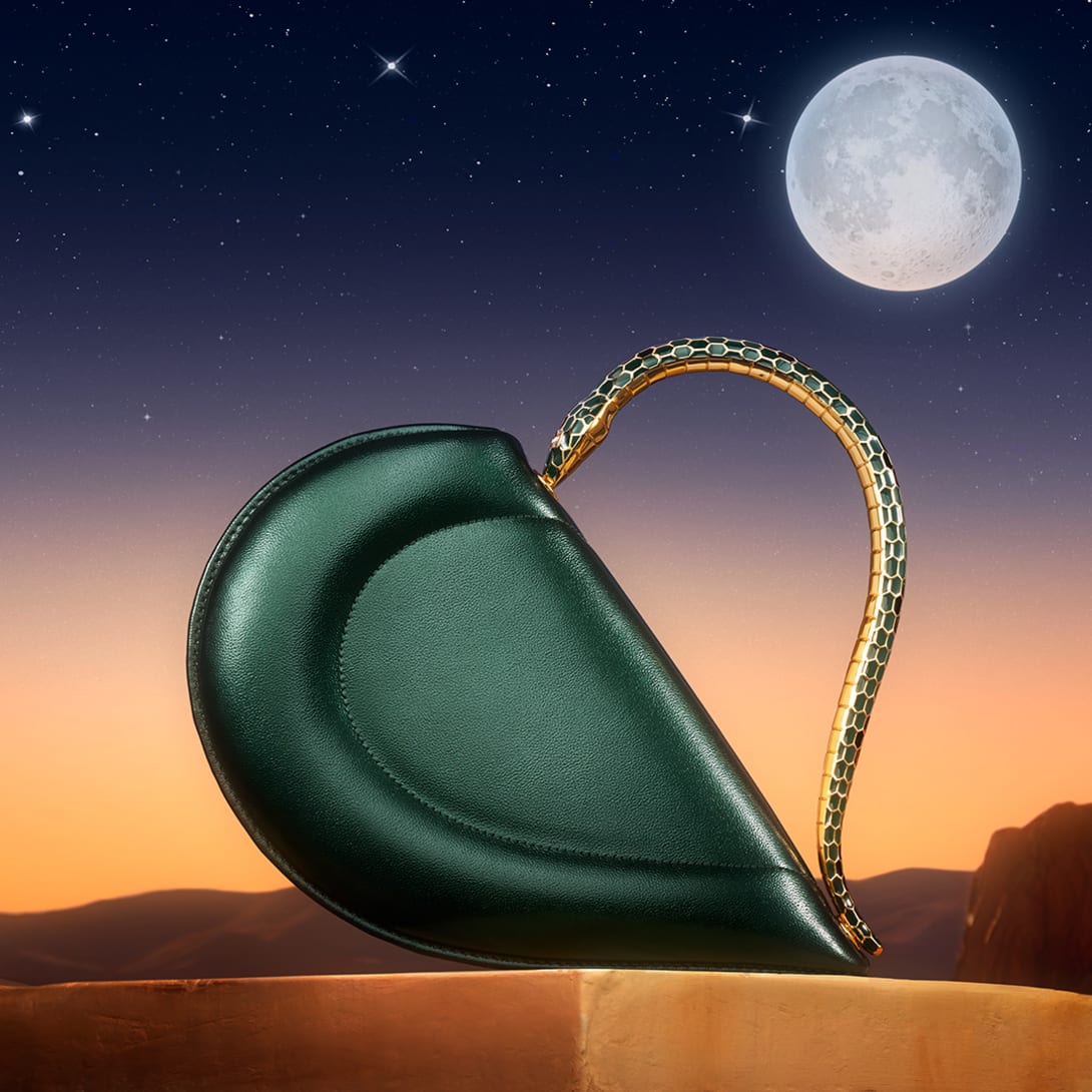 Bvlgari Cuore heart-shaped black leather bag with metallic snake handle set against a moonlit night sky.