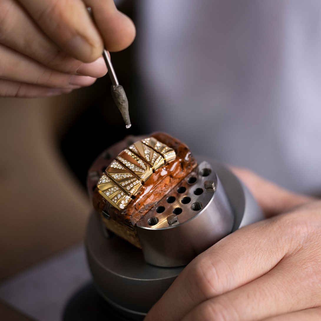 Tweezers holding a colored gemstone during the Tubogas Manchette watch gem-setting process.