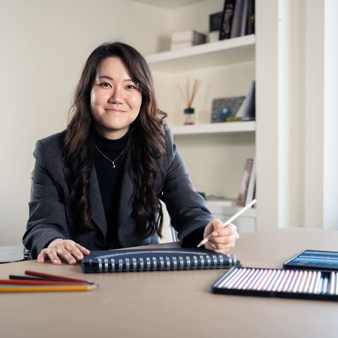 Sun Min, Senior Jewelry Designer, sorride alla fotocamera seduta alla scrivania