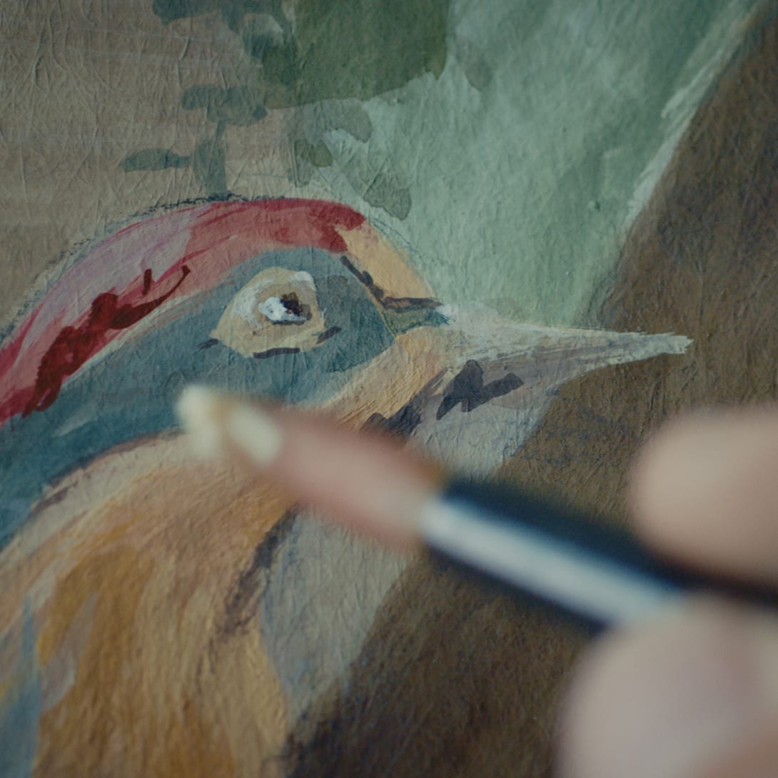 Craftsman hand-painting a colourful bird in the interior of the Bvlgari Hotel Rome, close-up.