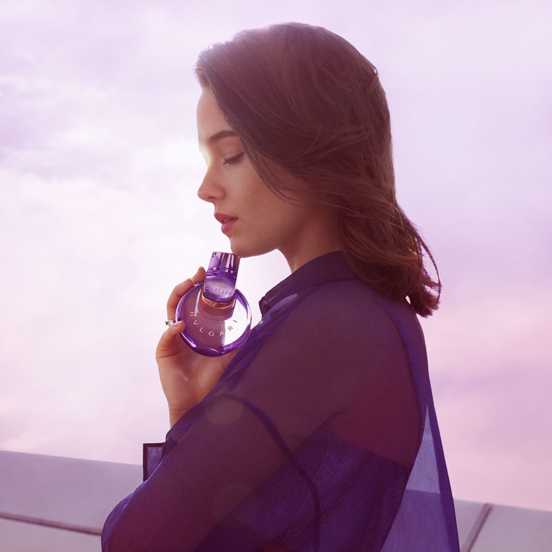 Bvlgari ambassador Cailee Spaeny holding the Omnia Amethyste fragrance bottle, purple sky backdrop.