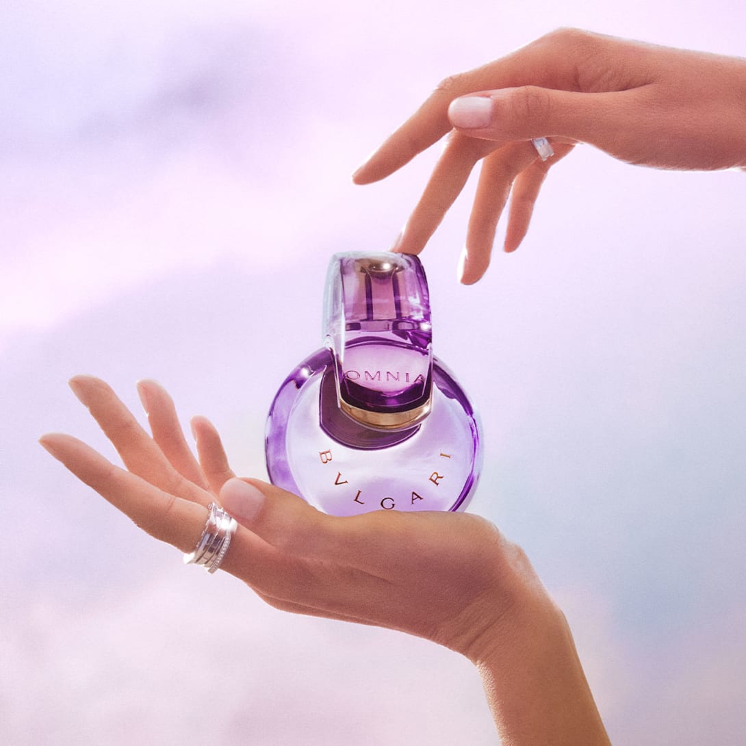 Purple Omnia Amethyste fragrance bottle in the infinity shape, purple backdrop, close-up.