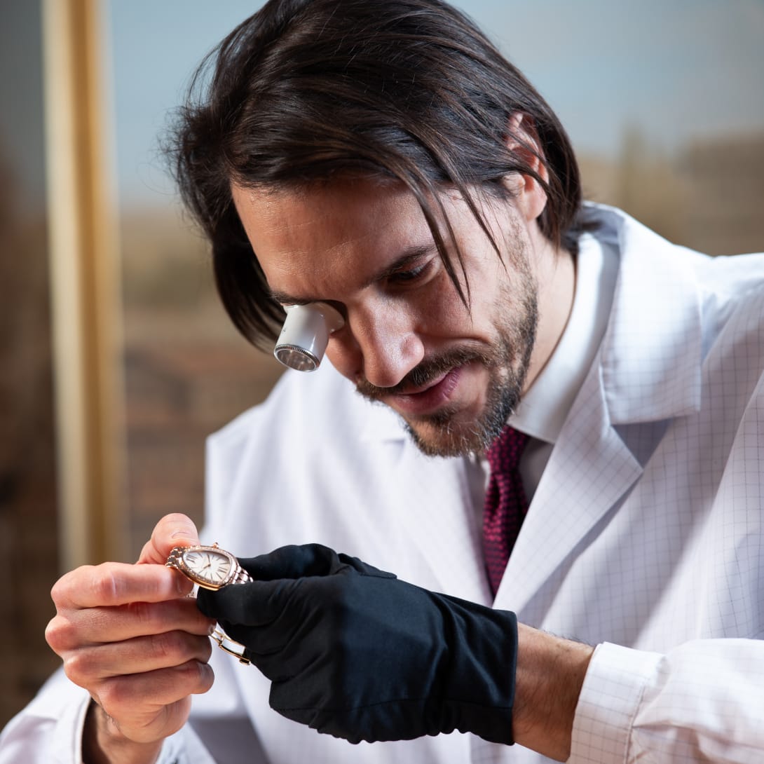 Un uomo in camice bianco esamina un orologio con un monocolo