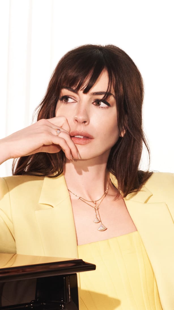 Anne Hathaway leaning against a piano and wearing a yellow gold Divas' Dream necklace and earrings.