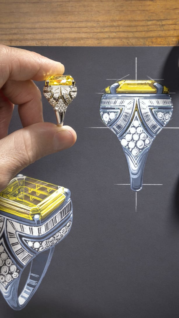 Artisan inserting a drop-shaped diamond in a High Jewellery necklace placed over a sketch, close-up.