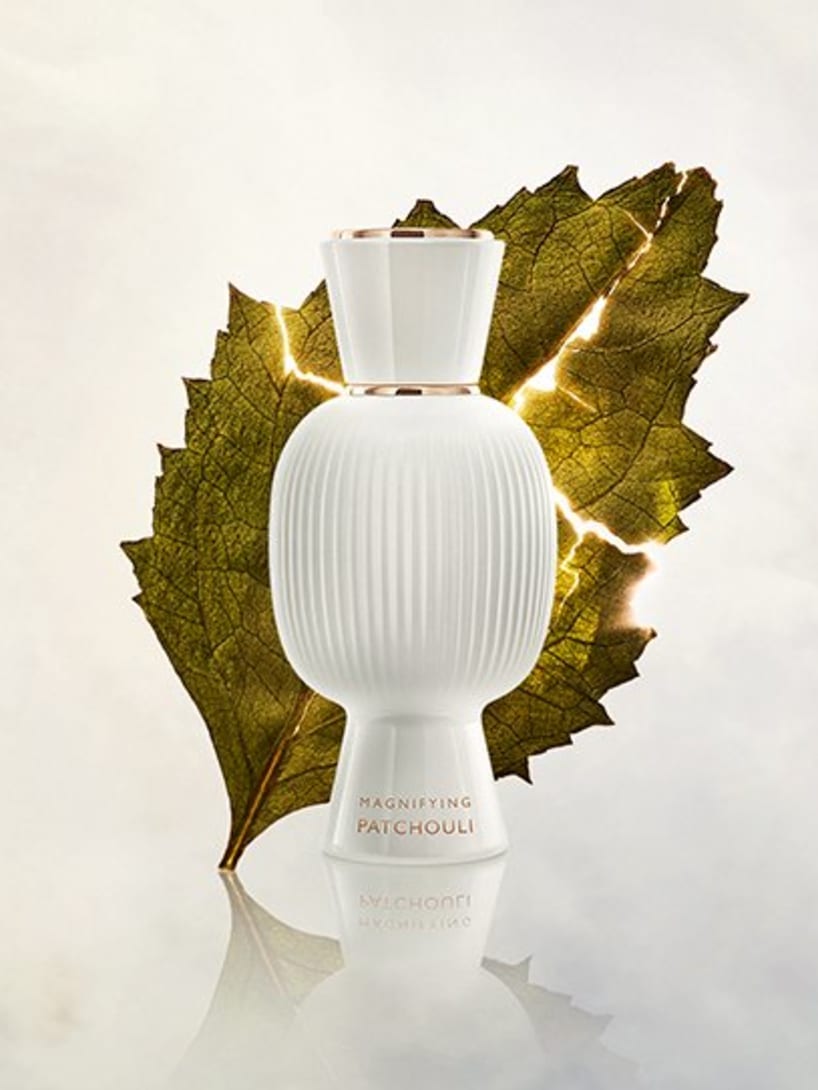 White flacon of the Bvlgari Allegra Magnifying Patchouli essence in front of a patchouli leaf, creative shot.