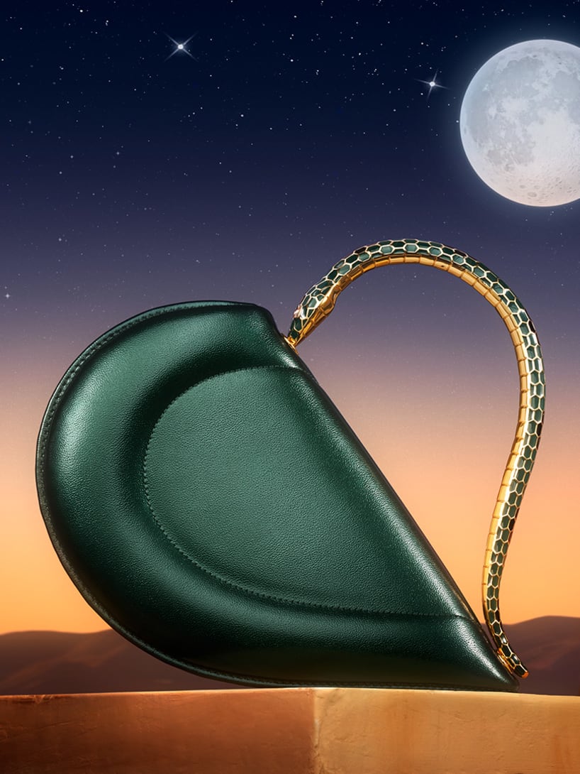Bvlgari Cuore heart-shaped black leather bag with metallic snake handle set against a moonlit night sky.