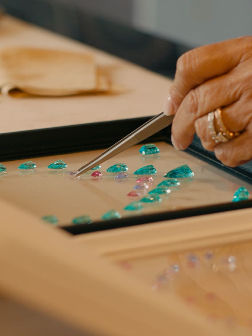Lucia Silvestri assembling precious gems on wax to design a necklace, close-up.