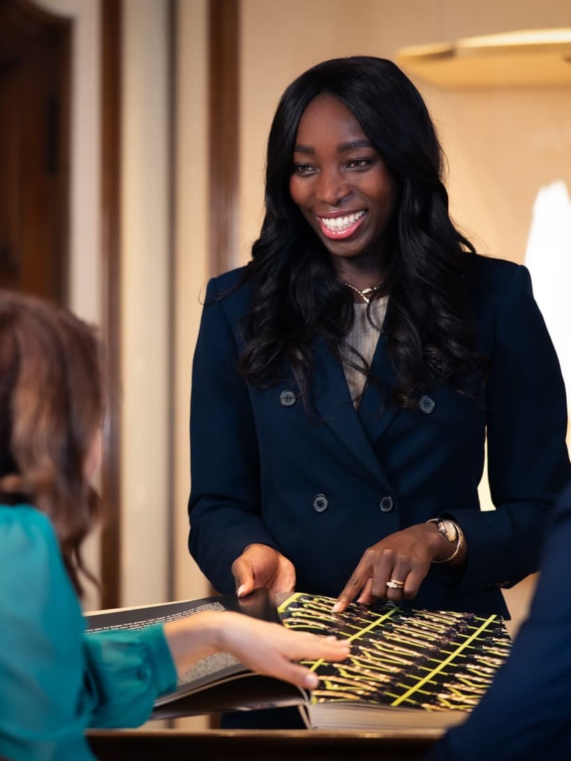 Satù, Store Manager presso Bvlgari, sfoglia un catalogo Bvlgari in compagnia di due colleghi, sorridendo