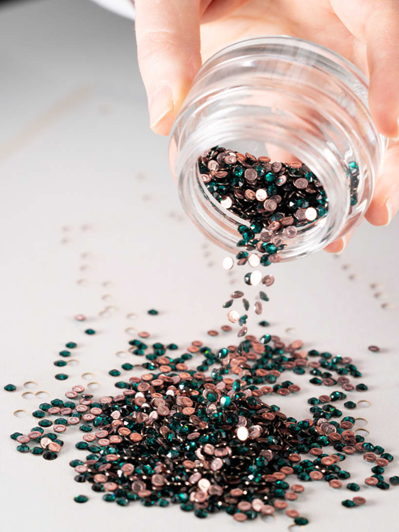 Craftsman emptying a jar of crystals for the workmanship of the Serpentine Duo tote bag, close up.
