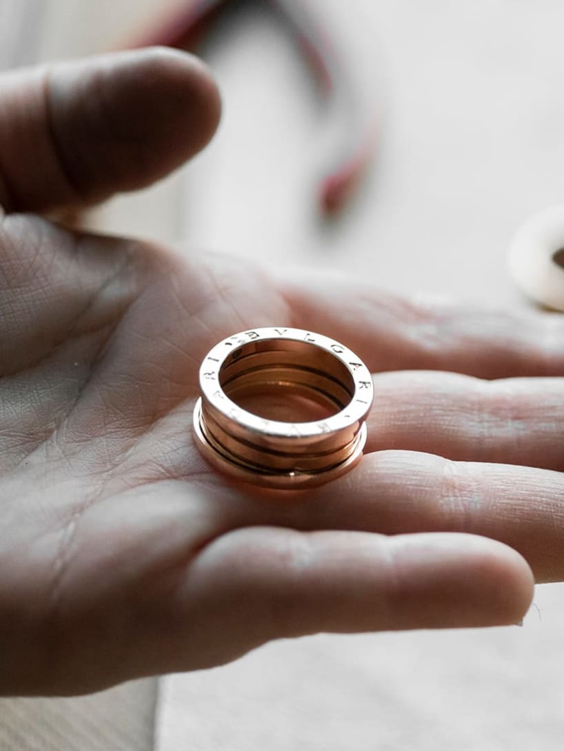 Hand holding a B.zero1 three-band gold ring, other rings and crafting tools in the back.