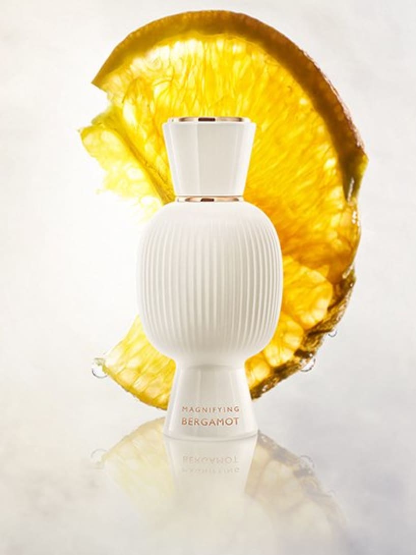 White flacon of the Bvlgari Allegra Magnifying Bergamot essence in front of a slice of bergamot, creative shot.