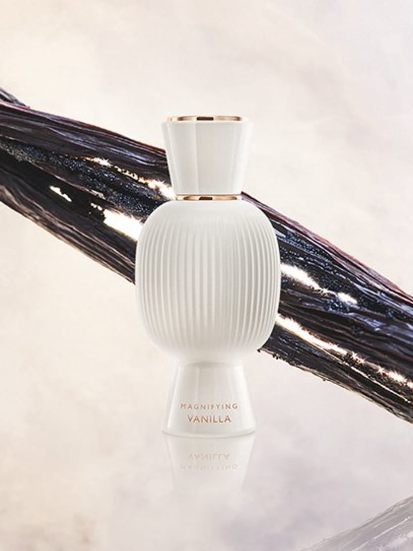 White flacon of the Bvlgari Allegra Magnifying Vanilla essence in front of vanilla beans, creative shot.