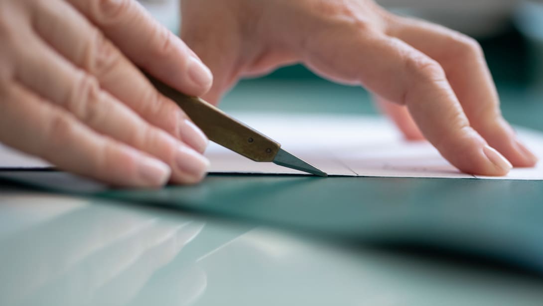 Bulgari artisan cutting a green calf leather panel for the making of a Bulgari handbag, close up on the hands.