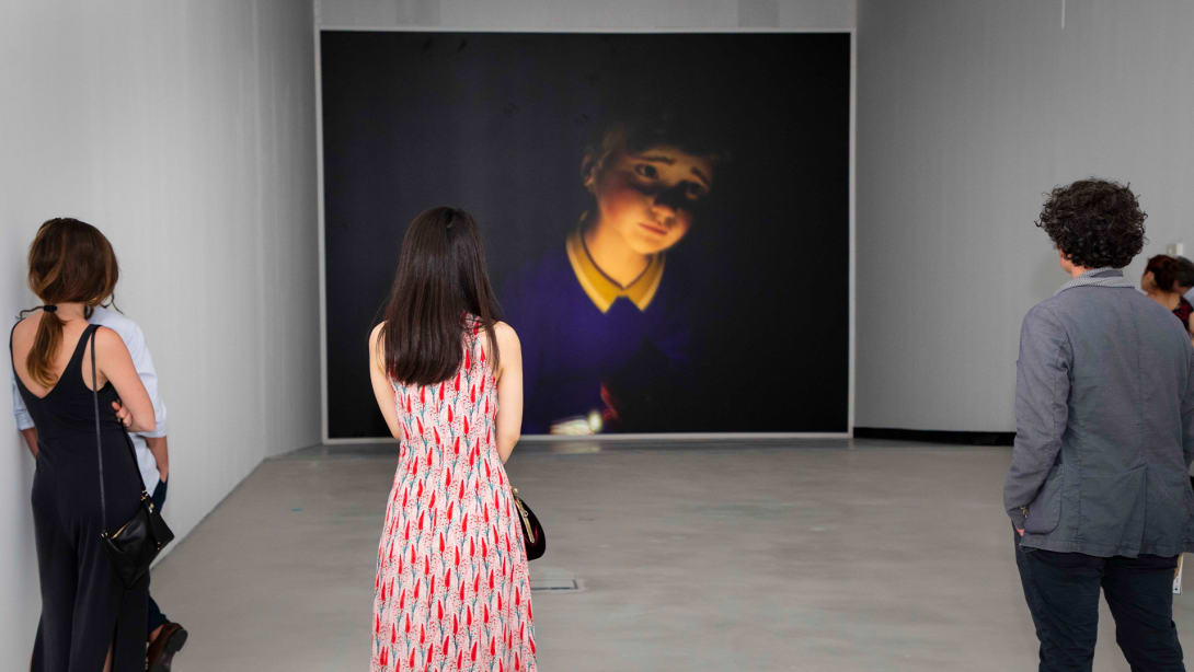 People from behind admiring a painting representing a person in a museum.