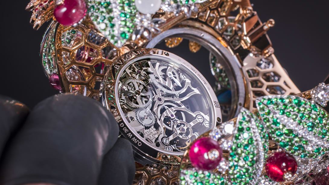 Hands with black gloves holding a High Jewellery watch in the making set with coloured gemstones.