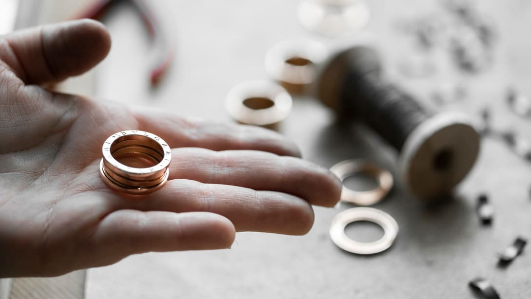 Hand holding a B.zero1 three-band gold ring, other rings and crafting tools in the back.