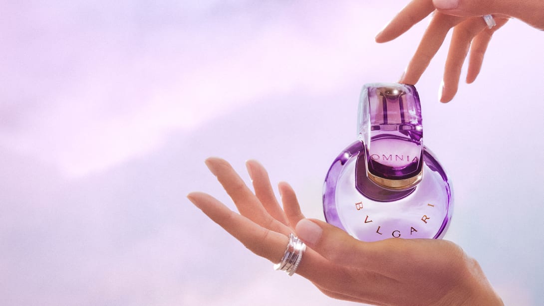 Purple Omnia Amethyste fragrance bottle in the infinity shape, purple backdrop, close-up