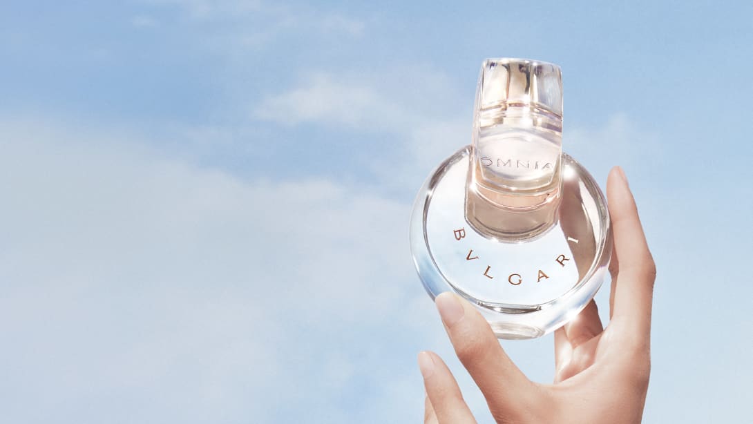 Transparent Omnia Crystalline fragrance bottle with Bulgari logo, sky backdrop, close-up