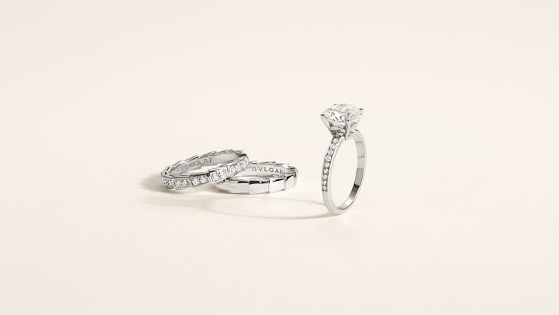 Bulgari engagement ring and wedding bands with solitaire ring on white backdrop.