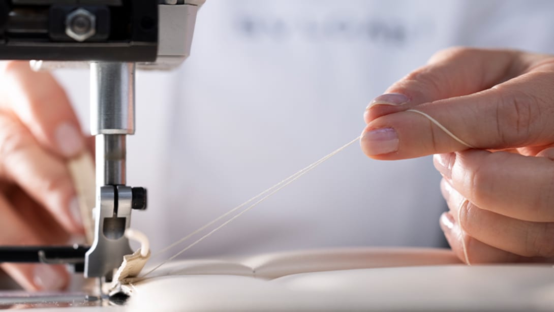 Bulgari craftsman sewing the white calf leather panel of a Serpenti handbag, close up.