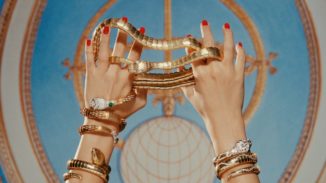 Serpenti heritage gold belt and secret watch with diamond head around two hands, fresco in the background.
