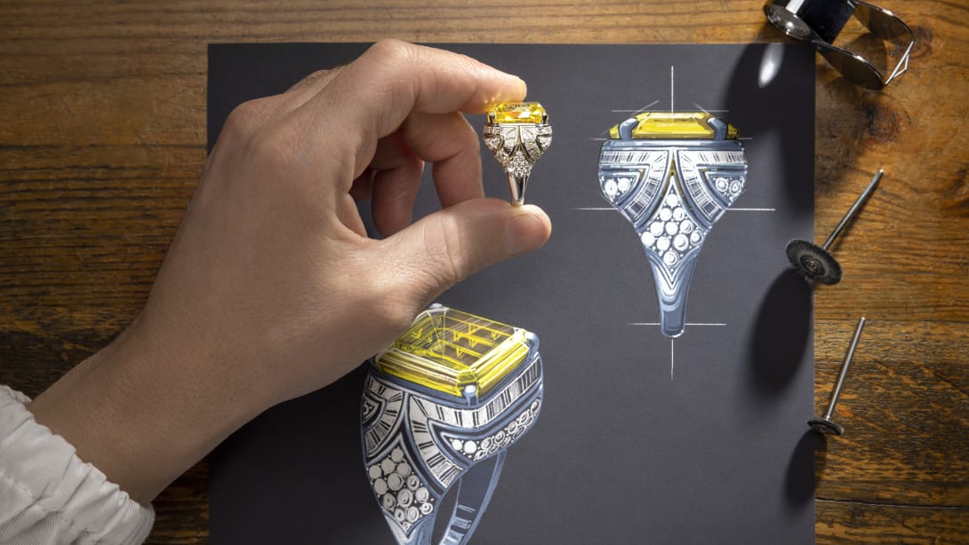 Artisan inserting a drop-shaped diamond in a High Jewellery necklace placed over a sketch, close-up.