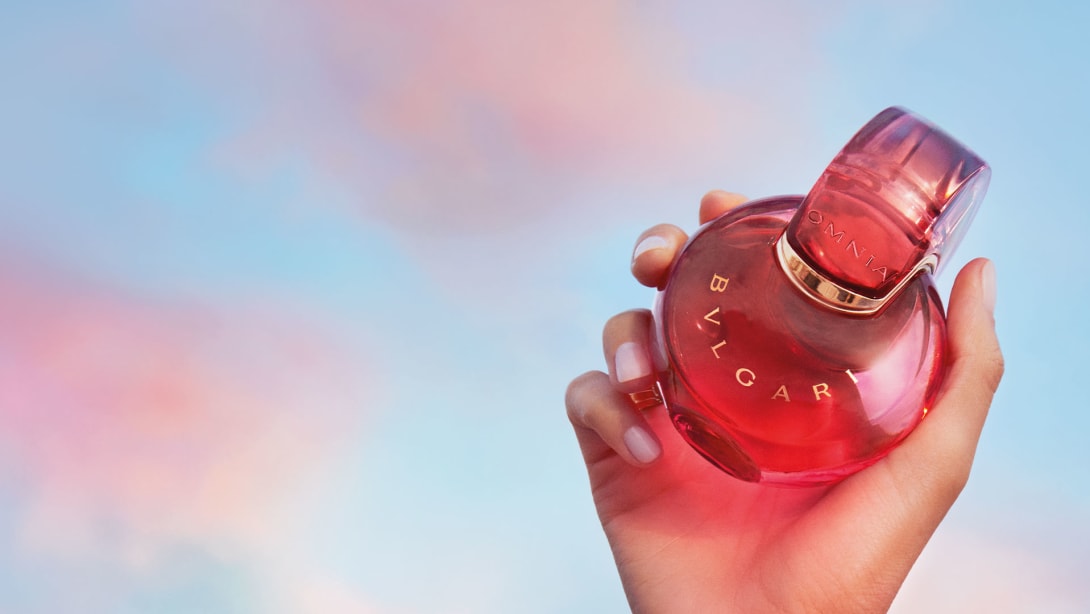 Red Omnia Coral fragrance bottle with Bulgari logo, red backdrop, close-up