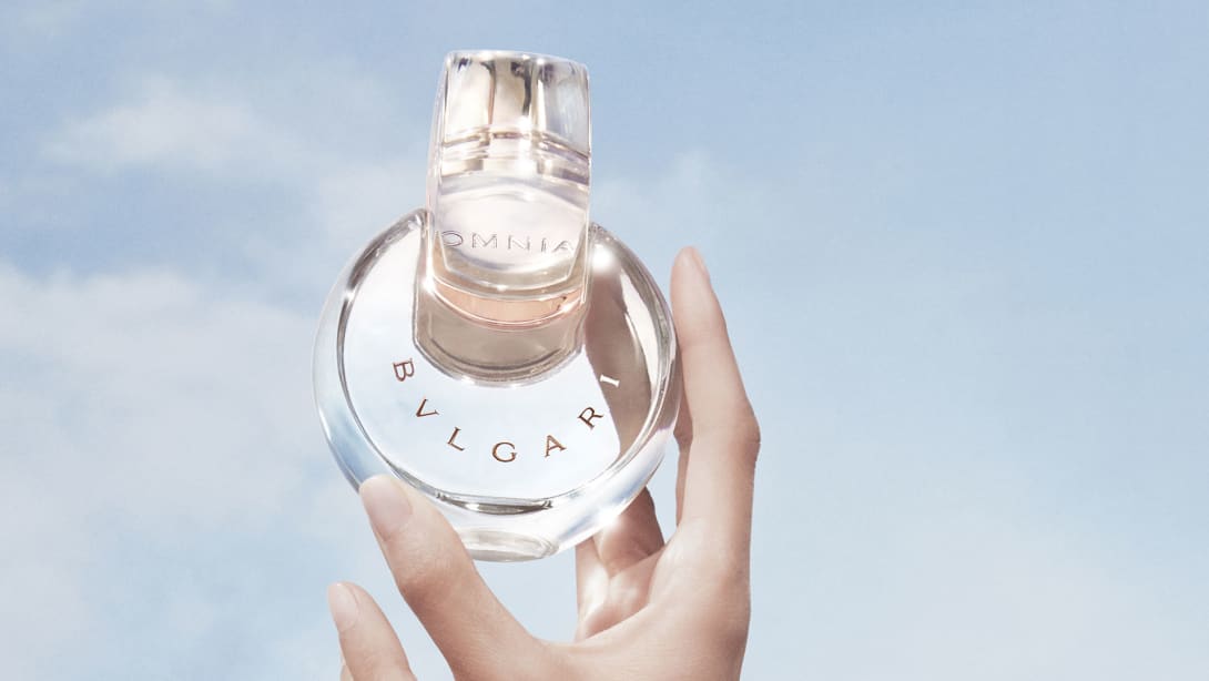 Transparent Omnia Crystalline fragrance bottle with Bulgari logo, sky backdrop, close-up