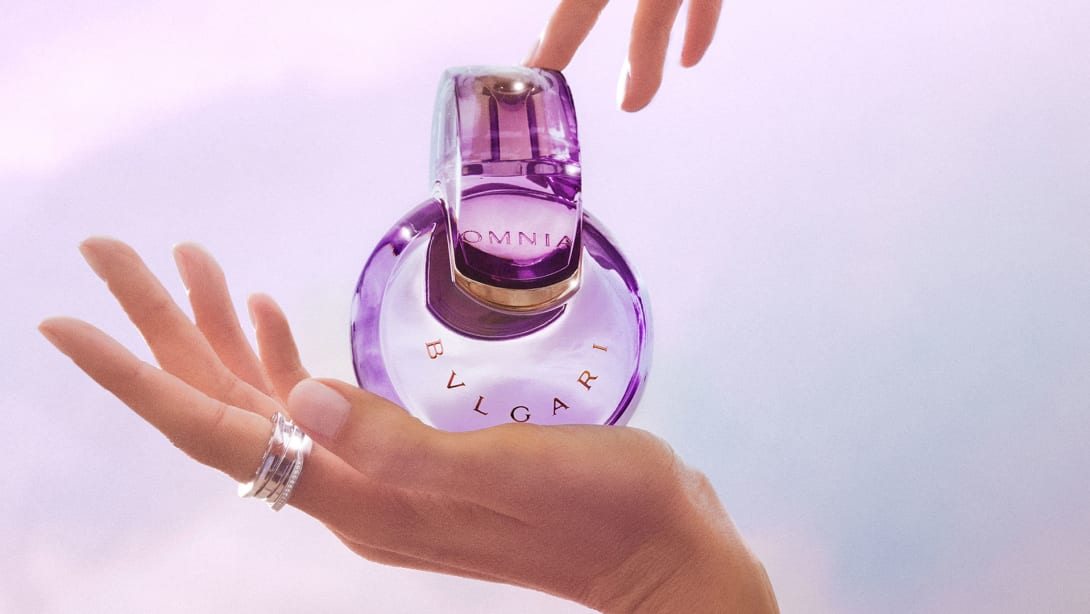 Purple Omnia Amethyste fragrance bottle in the infinity shape, purple backdrop, close-up