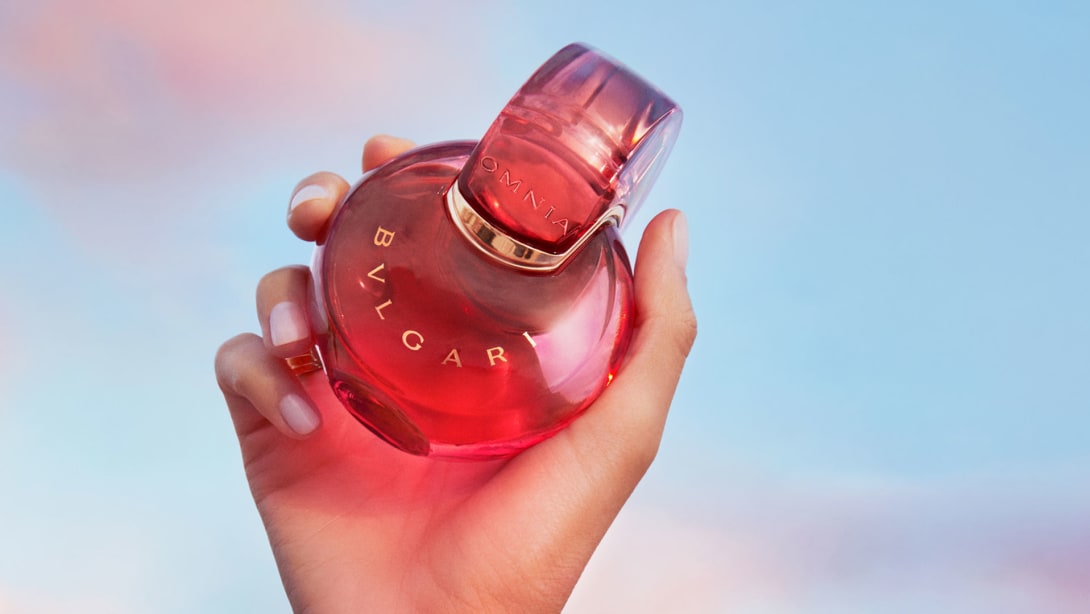 Red Omnia Coral fragrance bottle with Bulgari logo, red backdrop, close-up