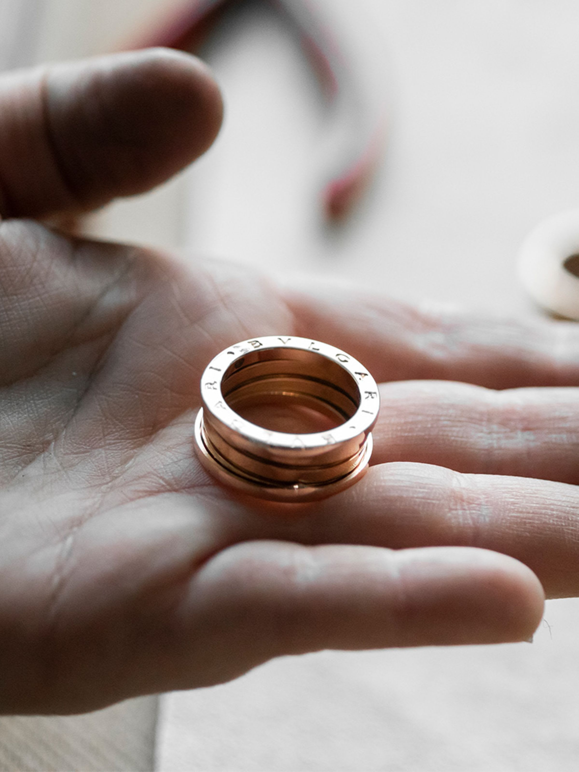 Hand holding a B.zero1 three-band gold ring, other rings and crafting tools in the back.