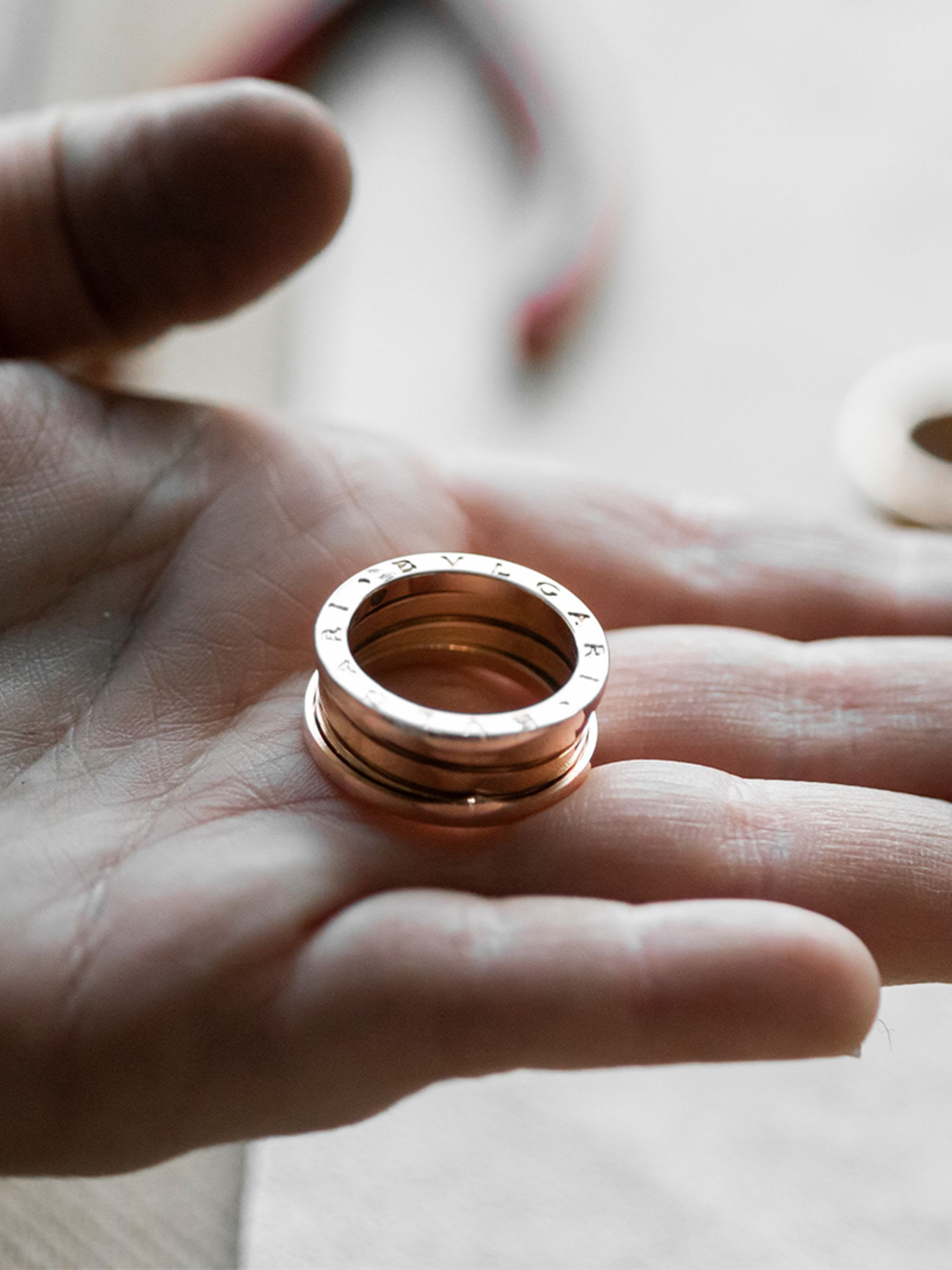 Hand holding a B.zero1 three-band gold ring, other rings and crafting tools in the back.