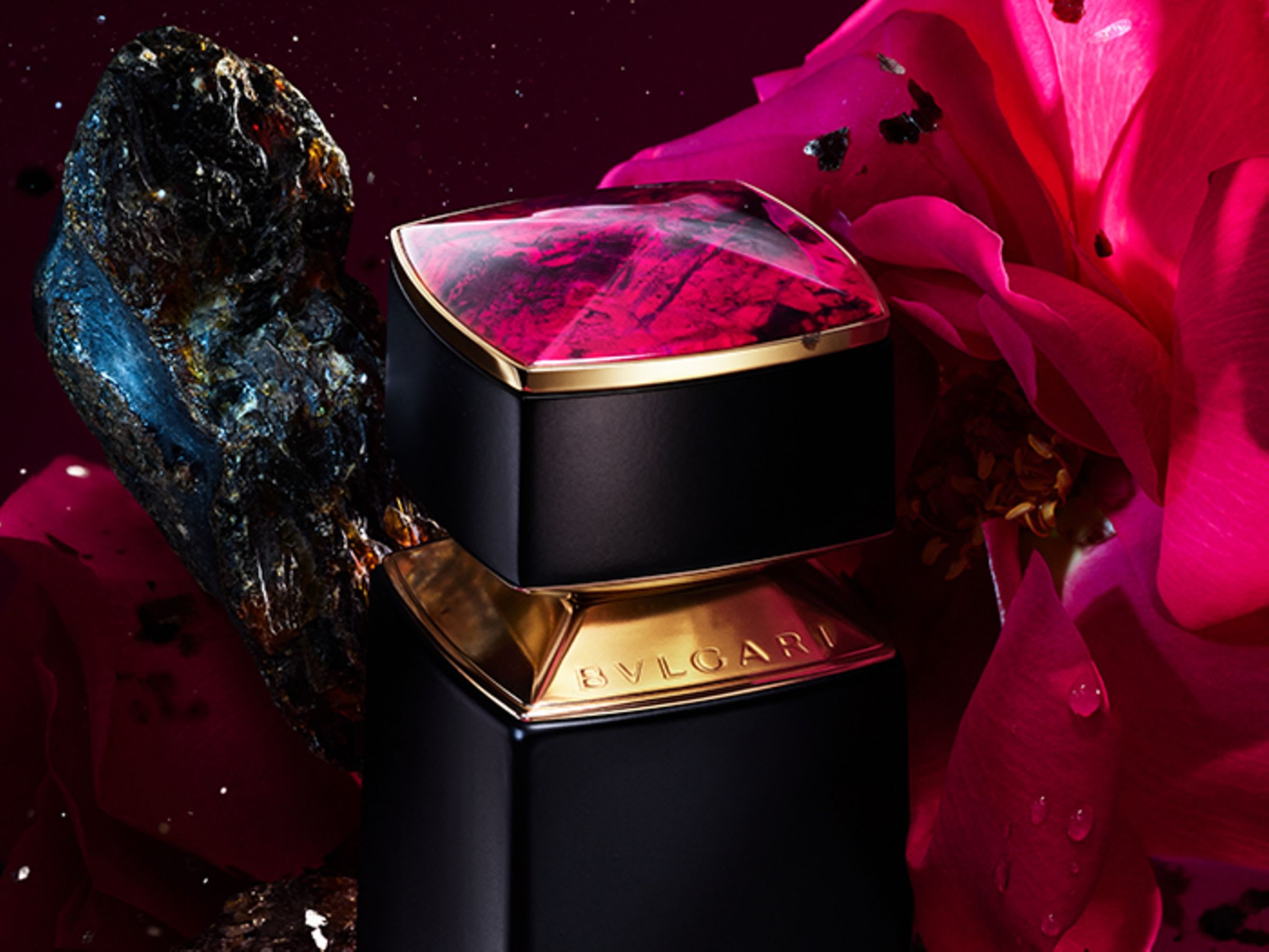 Pink cap of the Bvlgari Le Gemme Sahare fragrance, rose and ambergris in the back, close up.