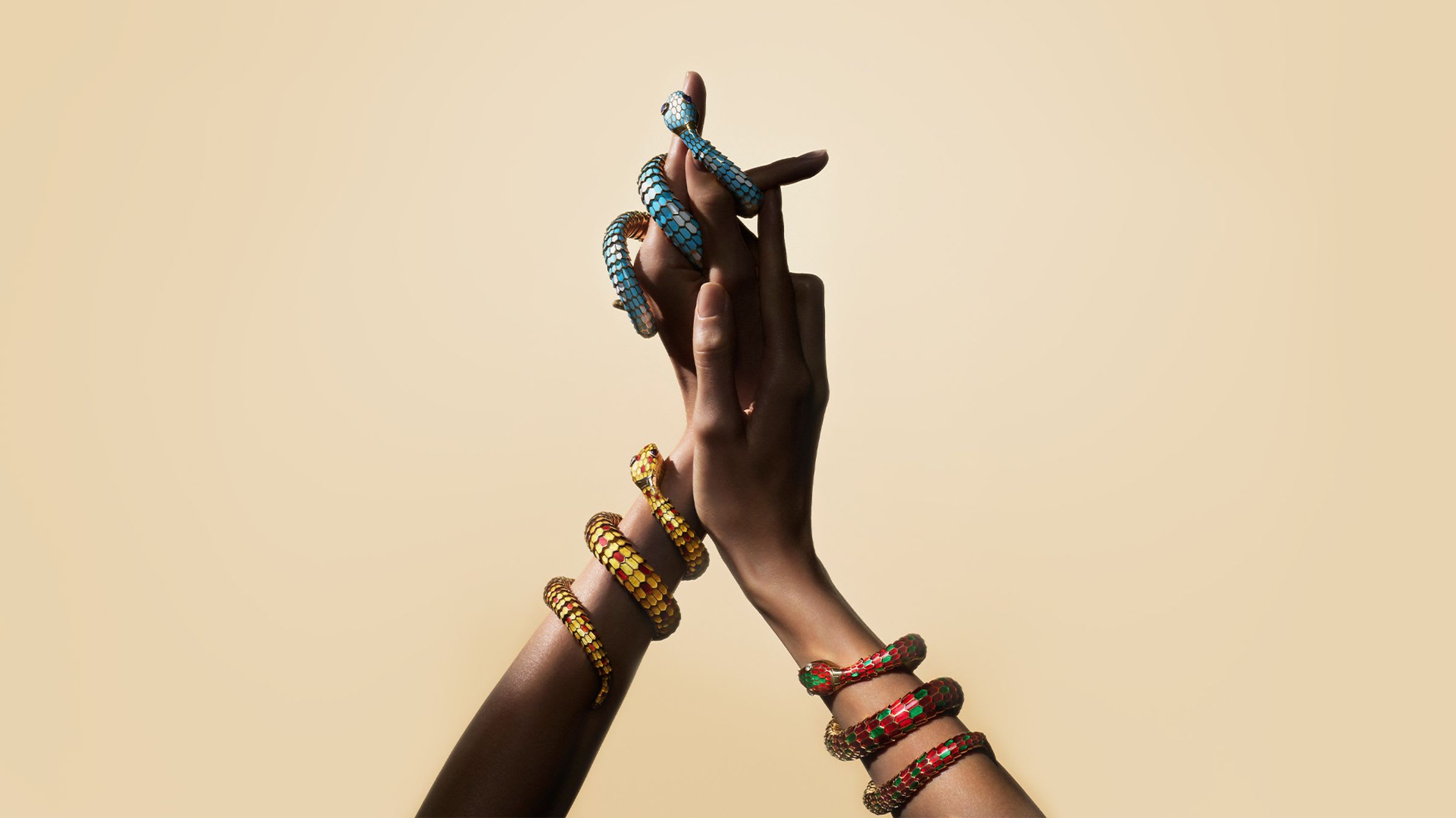 Two Serpenti heritage secret watches with enamel scales coiling around two hands, beige background.